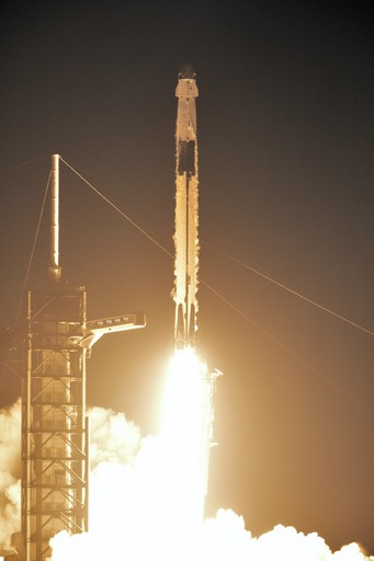 Photograph of a Falcon 9 rocket with a Crew Dragon capsule lifting off at night from LC-39A